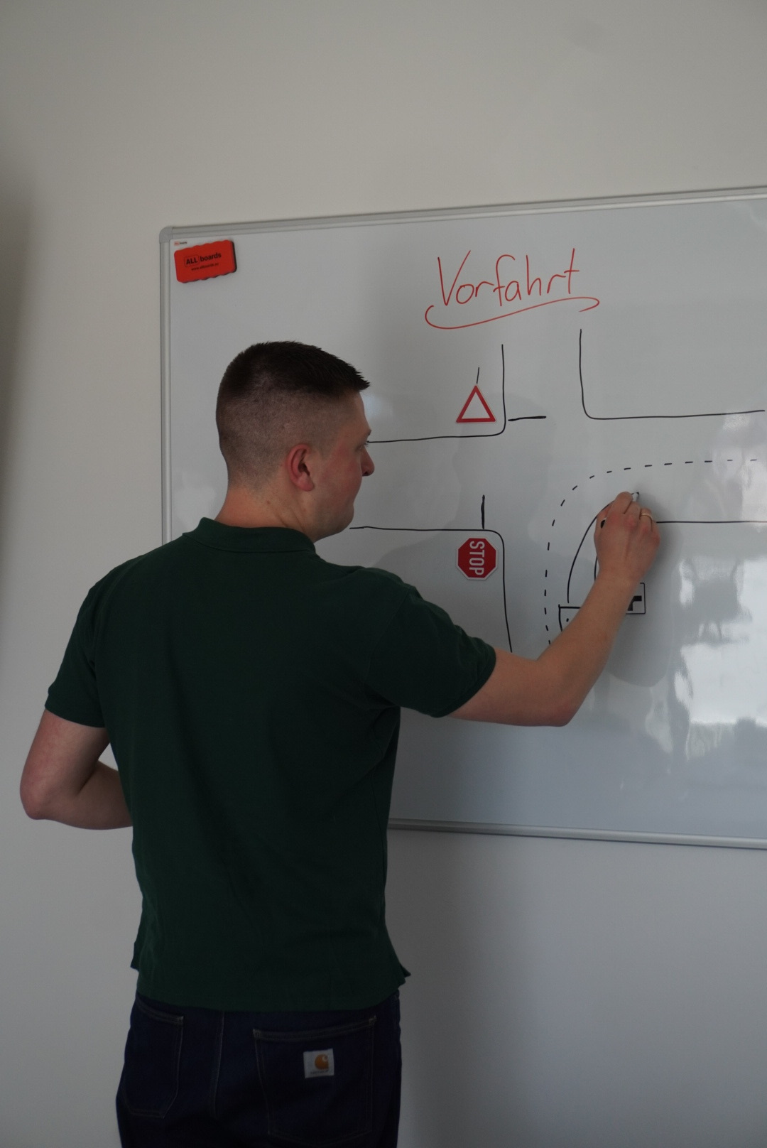 Ben von Fahrschule Abfahrt erklärt die Vorfahrt an einer Kreuzung an einer Tafel